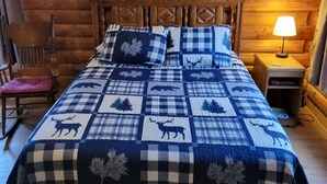 Un dormitorio de estilo cabaña de madera con una cama, una silla y una mesita de noche con una lámpara.