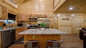Una cocina con armarios de madera, una isla central con asientos, electrodomésticos de acero inoxidable y una planta en maceta.