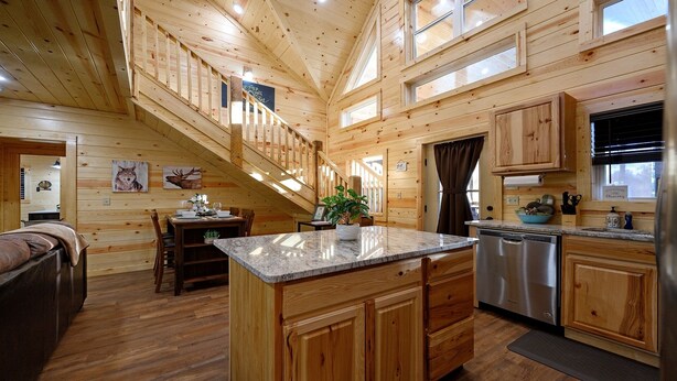 Interior de una cabaña con detalles de madera, un comedor, cocina y escalera.