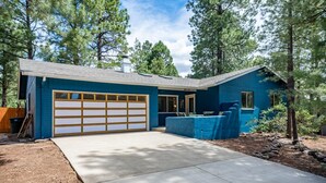 Una casa a due piani con facciata blu, un garage con porta in legno e un vialetto in cemento.