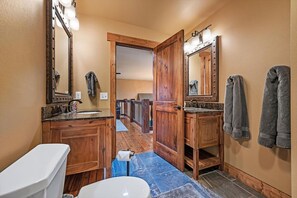 A bathroom with wooden cabinets, a sink, a toilet, and a large mirror with lights. - Gray Goose Lodge - Private back deck, hot tub and (Lead)
