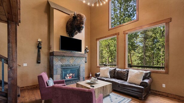 Ein gemütliches Wohnzimmer mit Kamin aus Stein, einem aufgehängten Bisonkopf und großen Fenstern mit Blick auf den Wald.