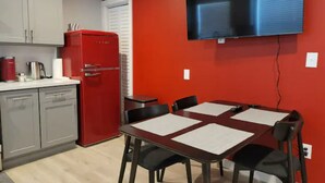 Cocina compacta con un refrigerador rojo, una mesa de comedor con cuatro sillas y un televisor de pantalla plana montado en la pared.