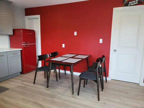 A compact kitchen with a red wall, a white door, and a red refrigerator.