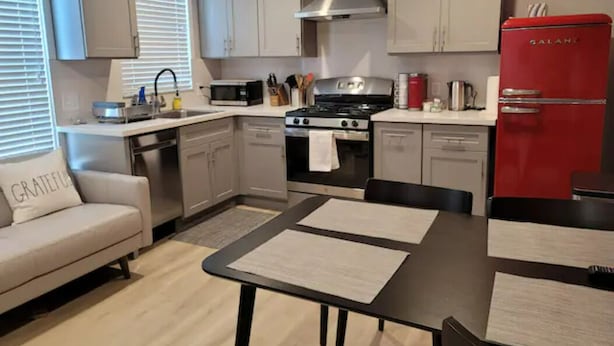 Una cocina moderna con gabinetes grises, un refrigerador rojo, una estufa a gas y un comedor con mesa y sillas.