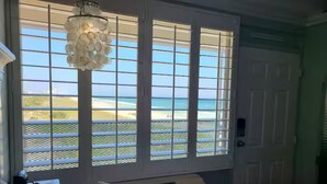 A bedroom with a large window overlooking a beach, a chandelier, and a bed with pillows. - Beachfront Studio • Gulf Views • Pool • Walk to Beach + Dining (Panama City Beach)