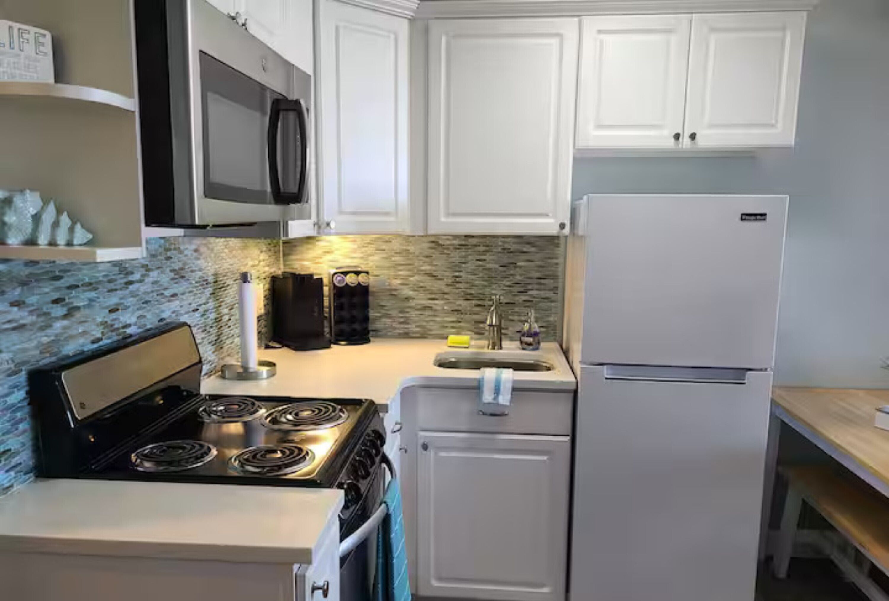 A compact kitchen with white cabinets, a black stove, a white refrigerator, and a tiled backsplash.