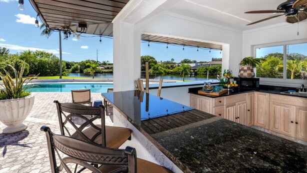 Cocina con vista a una piscina, mobiliario exterior y ventilador de techo.