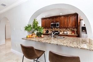 Una cocina con encimeras de granito, armarios de madera y un microondas de acero inoxidable, además de un lavabo.