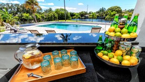 Zona de bar junto a la piscina, con vista despejada a una alberca, sillas de descanso y un paisaje tropical.