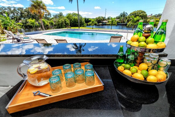 Zona de bar junto a la piscina, con vista despejada a una alberca, sillas de descanso y un paisaje tropical.