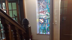 Un couloir avec un escalier en bois, une fenêtre à vitraux et une porte.