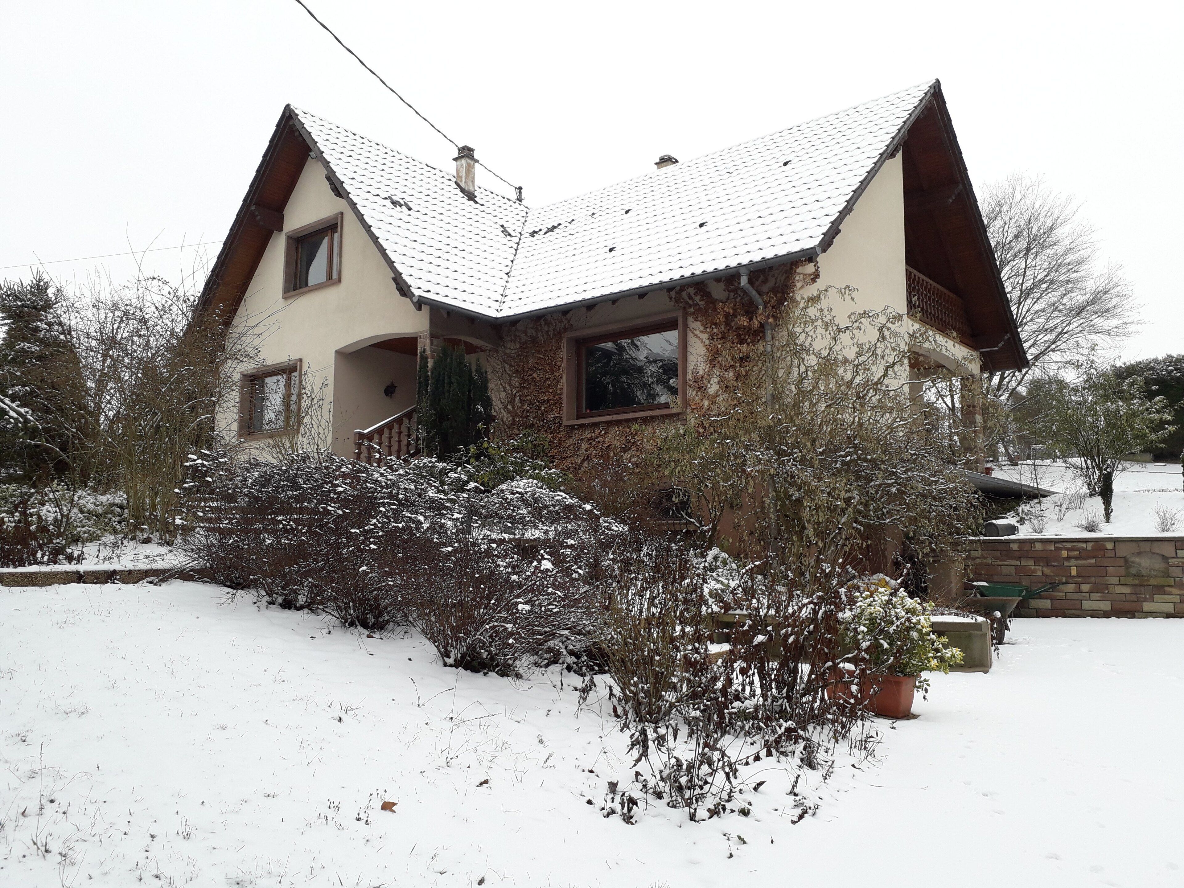 Ett tvåvåningshus med ett sluttande tak, en veranda och en snötäckt trädgård.
