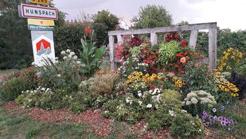 Un cartel con 'HUNSPACH' y 'D 249' señalando una ubicación, rodeado de una variedad de flores y plantas coloridas.