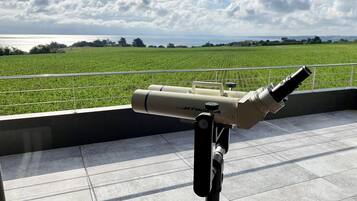 Un télescope sur un balcon, avec vue sur un champ verdoyant et la mer.