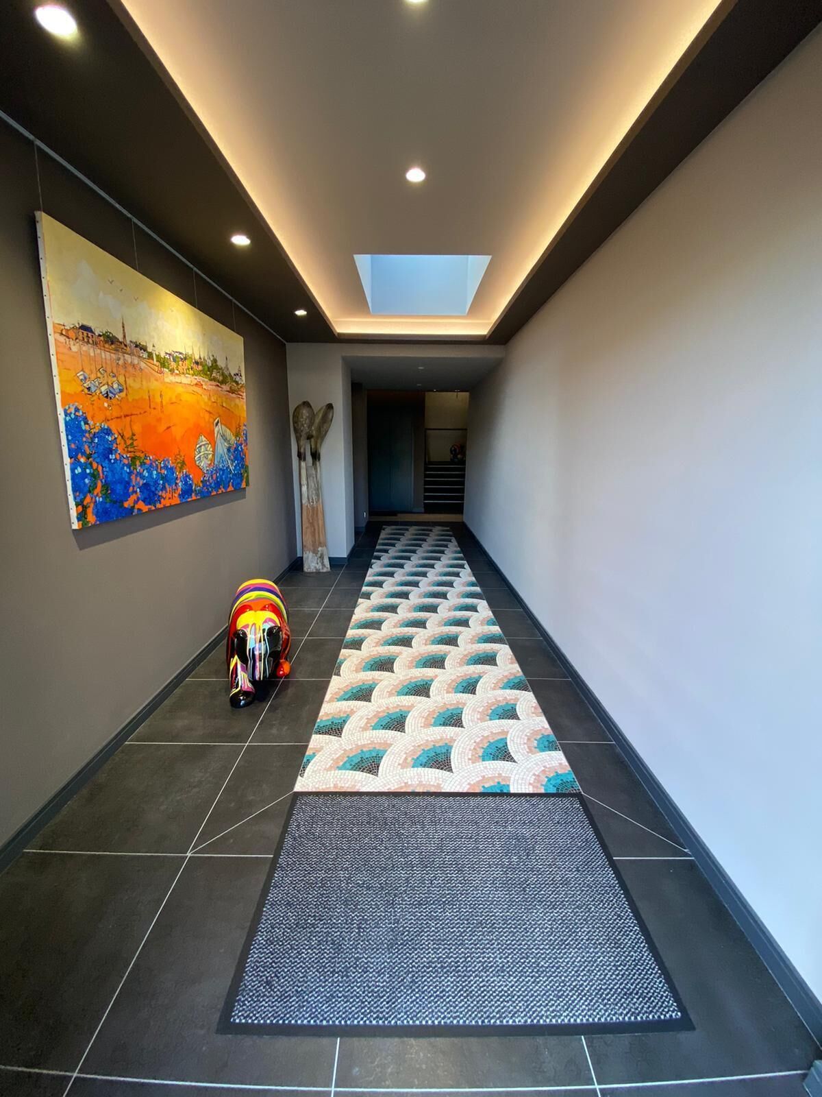 Un couloir moderne agrémenté d’une lucarne, d’un tableau aux couleurs vives et d’un tapis à motifs.