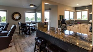 Una cocina moderna con una isla grande, encimeras oscuras y un comedor con sillas de cuero.