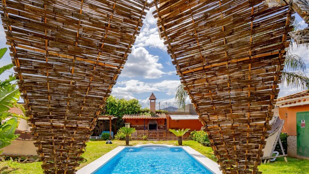 A swimming pool with a clear blue water, surrounded by a grassy area and a bamboo fence. - Cubo's Villa Lula (Cártama)