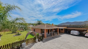 A residential property with a tiled roof, a covered patio, a fenced yard, and a parking area with a white van. - Cubo's Villa Lula (Cártama)