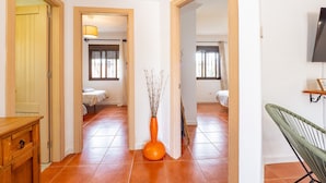 A hallway with a wooden cabinet, a vase with branches, and a chair. - Cubo's Villa Lula (Cártama)