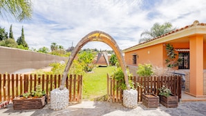 An outdoor entrance with a wooden archway, stone flooring, and a fenced garden area. - Cubo's Villa Lula (Cártama)