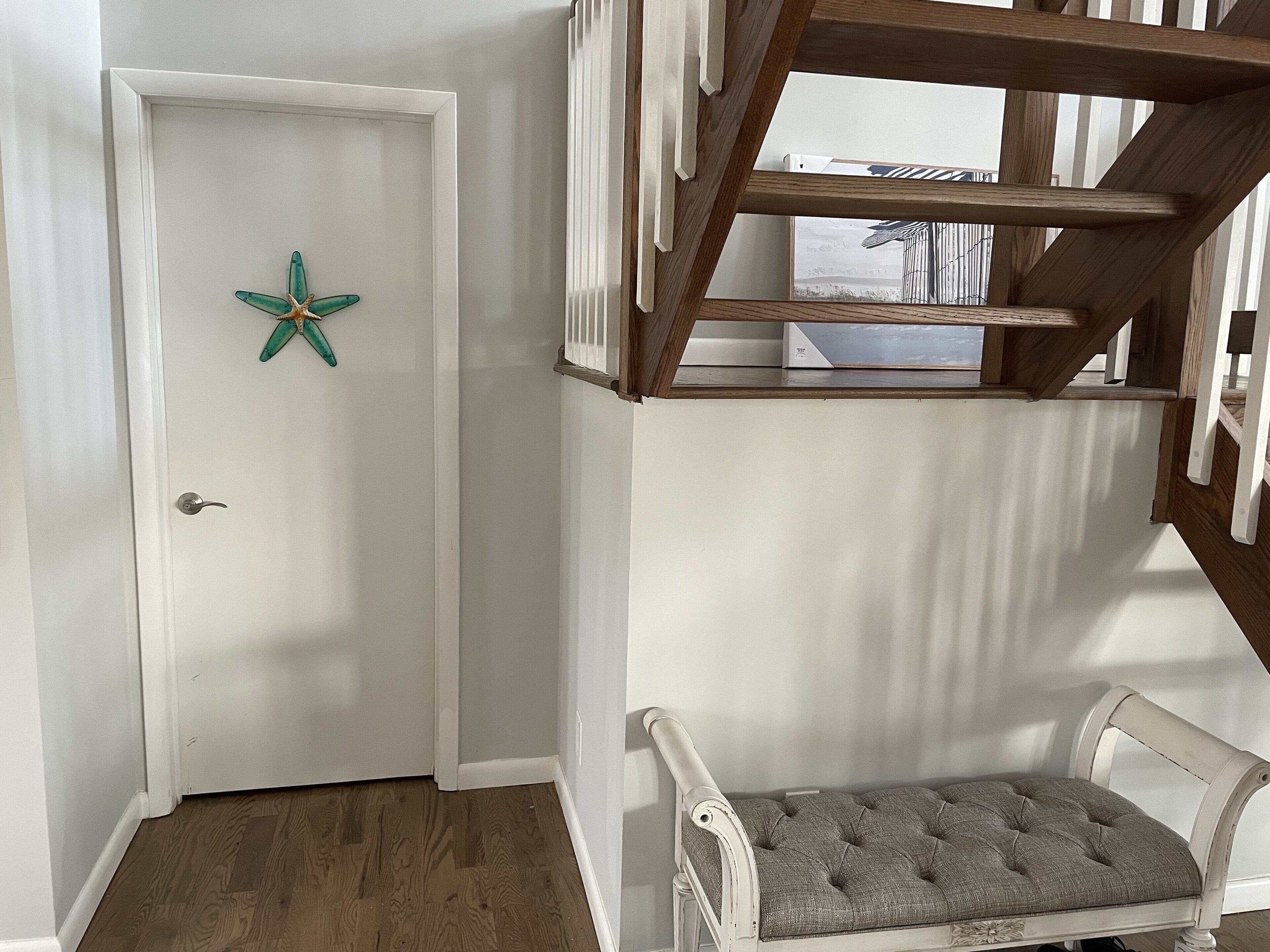 A white door with a starfish decoration, a wooden staircase, and a cushioned bench.
