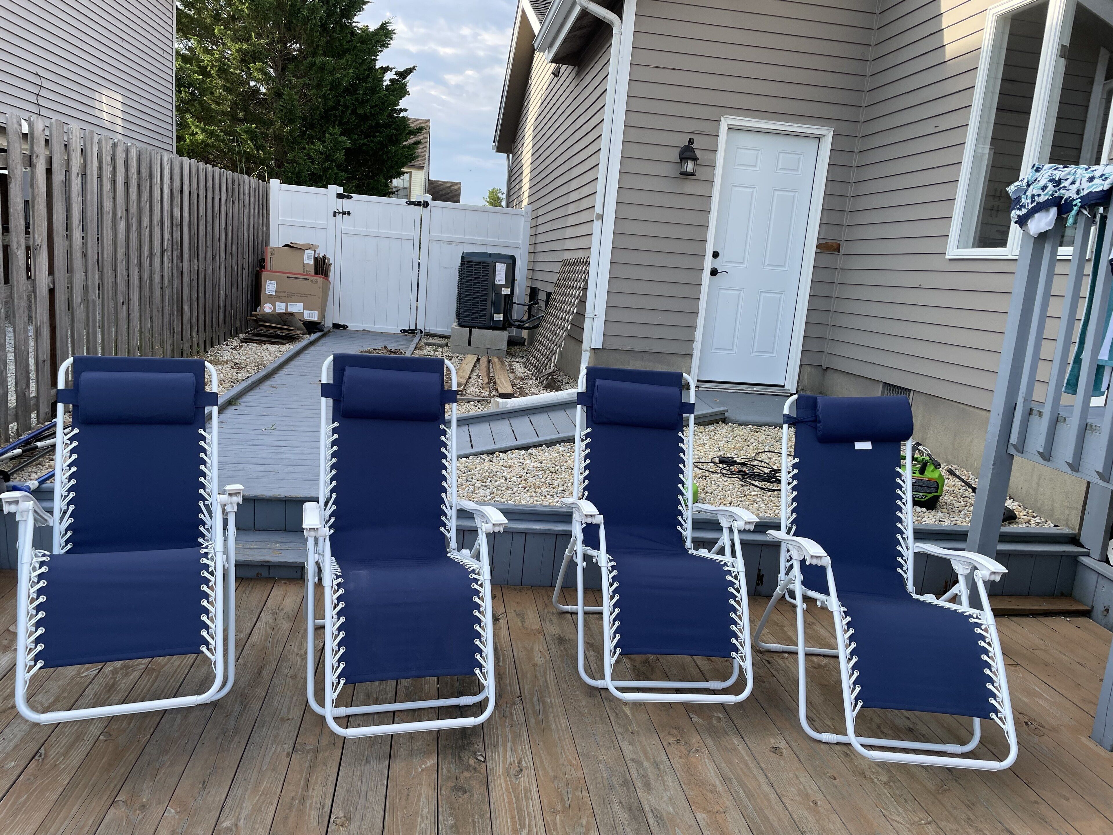 A deck with four blue lounge chairs and a white door.