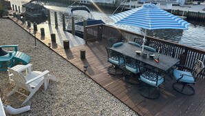 A waterfront deck with a table and chairs, a dock with boats, and houses in the background.