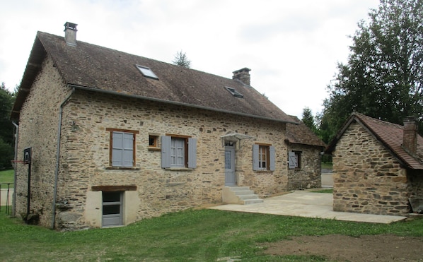 A stone house with a sloped roof, a small porch, and a door leading to the entrance.