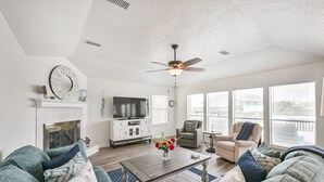 Un salon spacieux doté d’une cheminée, d’un ventilateur de plafond et de grandes fenêtres.
