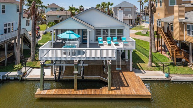 Une maison située au bord de l’eau, dotée d’une terrasse en bois, d’un espace extérieur aménagé et couvert, et offrant une vue sur l’eau.