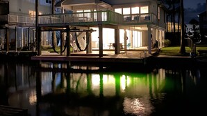 Une propriété située au bord de l’eau, dotée d’une terrasse couverte, d’une piscine et d’une maison à deux étages avec de grandes fenêtres et un balcon.