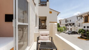 A balcony with a chair and table, a sliding glass door, and a view of a street with parked cars and buildings. - 5 Min Driving to he Beach, 6 People, 5 Beds, Pool, wifi (Playa del Carmen)