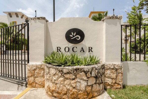 Une enseigne portant le nom « ROCAR » et un logo, le tout entouré d’un mur de pierres et d’un portail en métal.