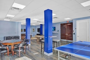 A room with a ping pong table, a pool table, and a dining area with chairs and a table.