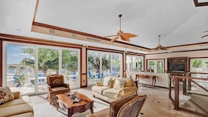 A spacious living area with a large sliding glass door leading to a balcony, a ceiling fan, and a television. - Key Largo Luxury Townhome | Pools & Marina (Key Largo)