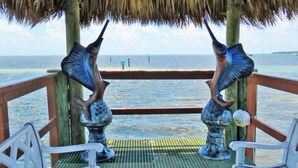 A wooden deck with a thatched roof, two bird sculptures, and a view of the ocean. - Key Largo Luxury Townhome | Pools & Marina (Key Largo)