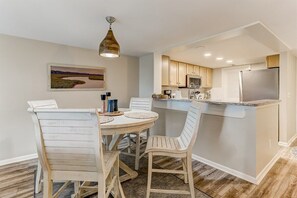 A compact kitchen with a central island, white cabinetry, and a dining area with a round table and chairs.