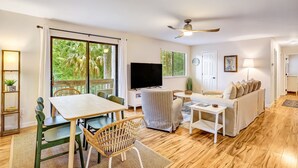 A spacious living area with a dining table, chairs, a sofa, a TV, and a ceiling fan. - Ace the Day:  Pool, Tennis, & Pickleball Fun (Fernandina Beach)