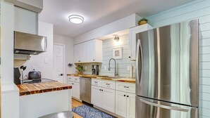 A compact kitchen with white cabinets, a stainless steel refrigerator, a wooden countertop, and a blue rug. - Ace the Day:  Pool, Tennis, & Pickleball Fun (Fernandina Beach)