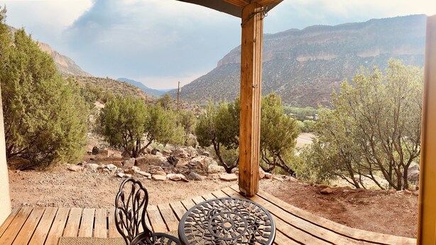 Une terrasse en bois avec une table et des chaises, offrant une vue sur un paysage montagneux à la végétation clairsemée.
