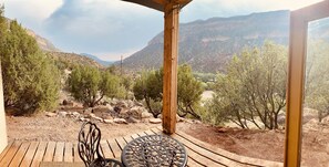 A wooden deck with a table and chairs, overlooking a mountainous landscape with sparse vegetation. - Mountain Adobe Home in Jemez Springs NEW HOT TUB, Mt. Views "Raven House" (Jemez Springs)