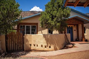 A stucco house with a wooden gate, a blue door, and a mountain backdrop. - Mountain Adobe Home in Jemez Springs NEW HOT TUB, Mt. Views "Raven House" (Jemez Springs)