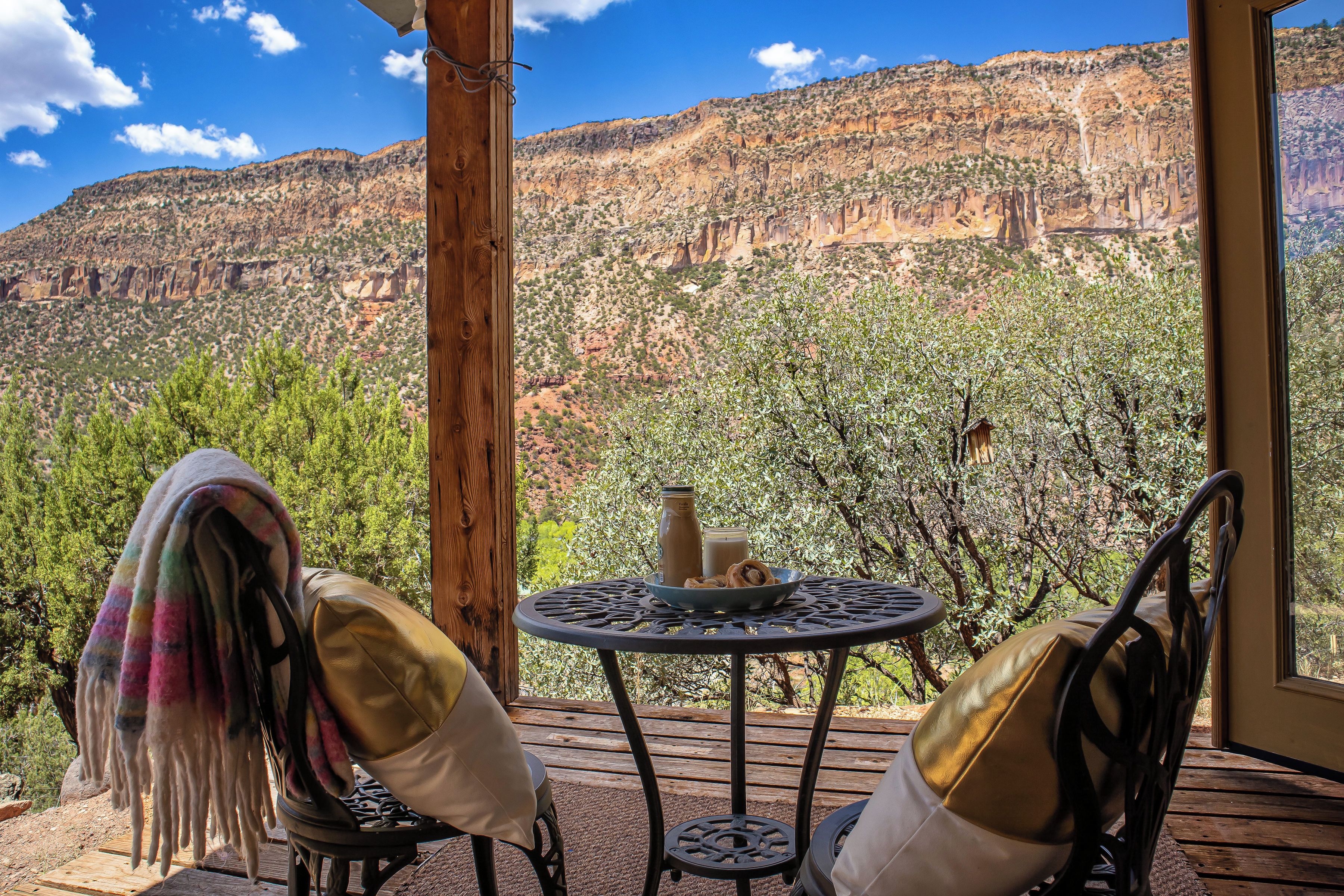 Una terraza de madera con una mesa y sillas, con vistas a un paisaje montañoso.