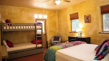 A room with bunk beds, a desk, a chair, a bed with a colorful blanket, a ceiling fan, and a window with blinds.