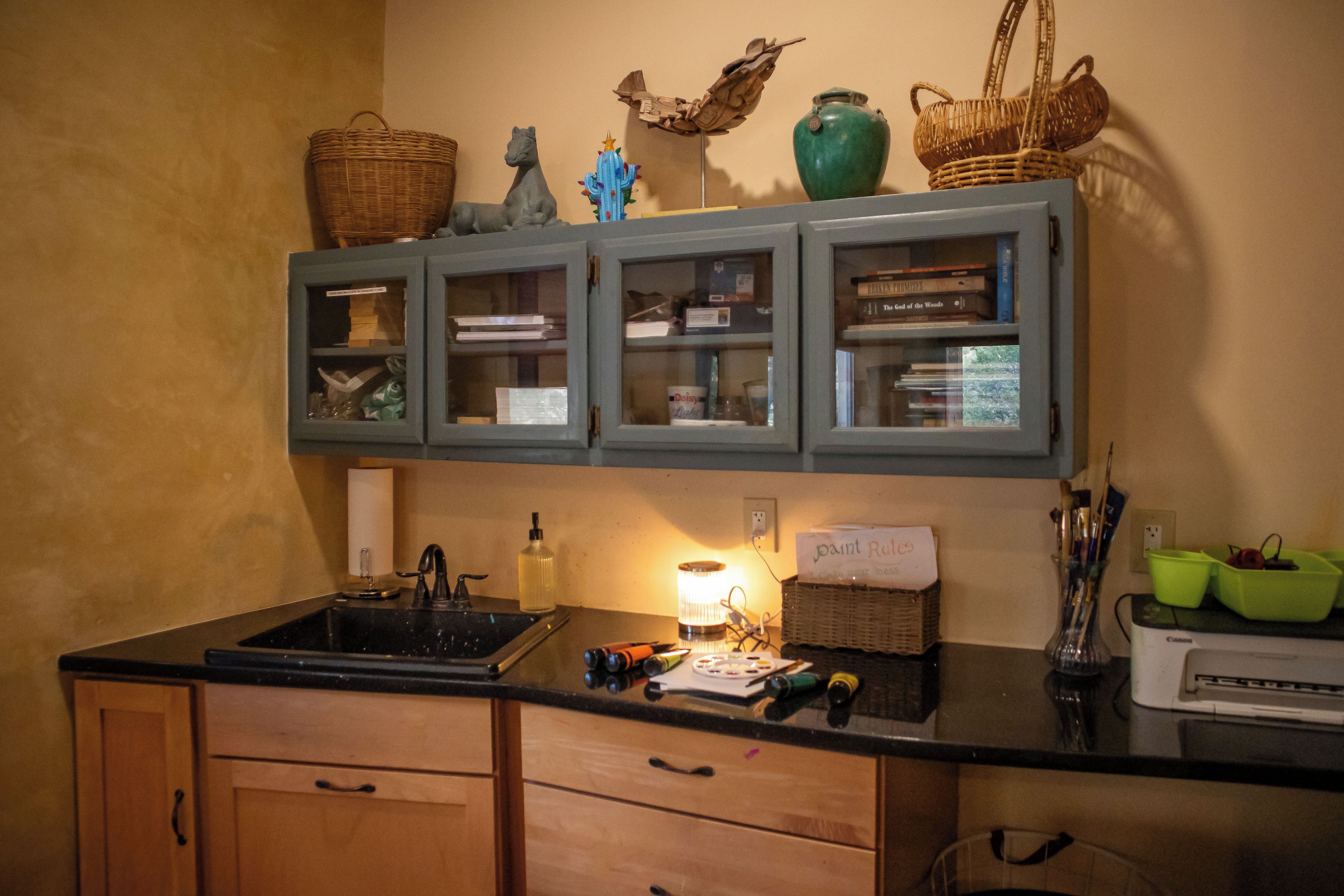 A kitchen with a black countertop, wooden cabinets, and a built-in shelf with decorative items.