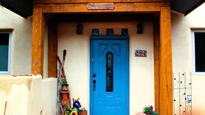 A building with a blue door, wooden porch, and a sign above the door. - Mountain Adobe Home in Jemez Springs NEW HOT TUB, Mt. Views "Raven House" (Jemez Springs)