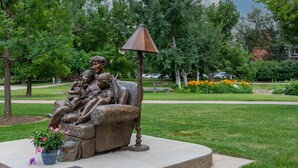 Eine Bronzestatue einer Familie, die auf einer Bank in einem Park sitzt, mit einem Laternenpfahl in der Nähe.