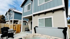 Ein zweistöckiges Haus mit einer Terrassenanlage, inklusive Whirlpool, Grill und Gartenmöbeln.