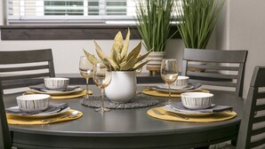Ein Esstisch ist gedeckt mit weißen Schüsseln, goldenen Platzsets und einer weißen Vase mit Grünpflanzen.